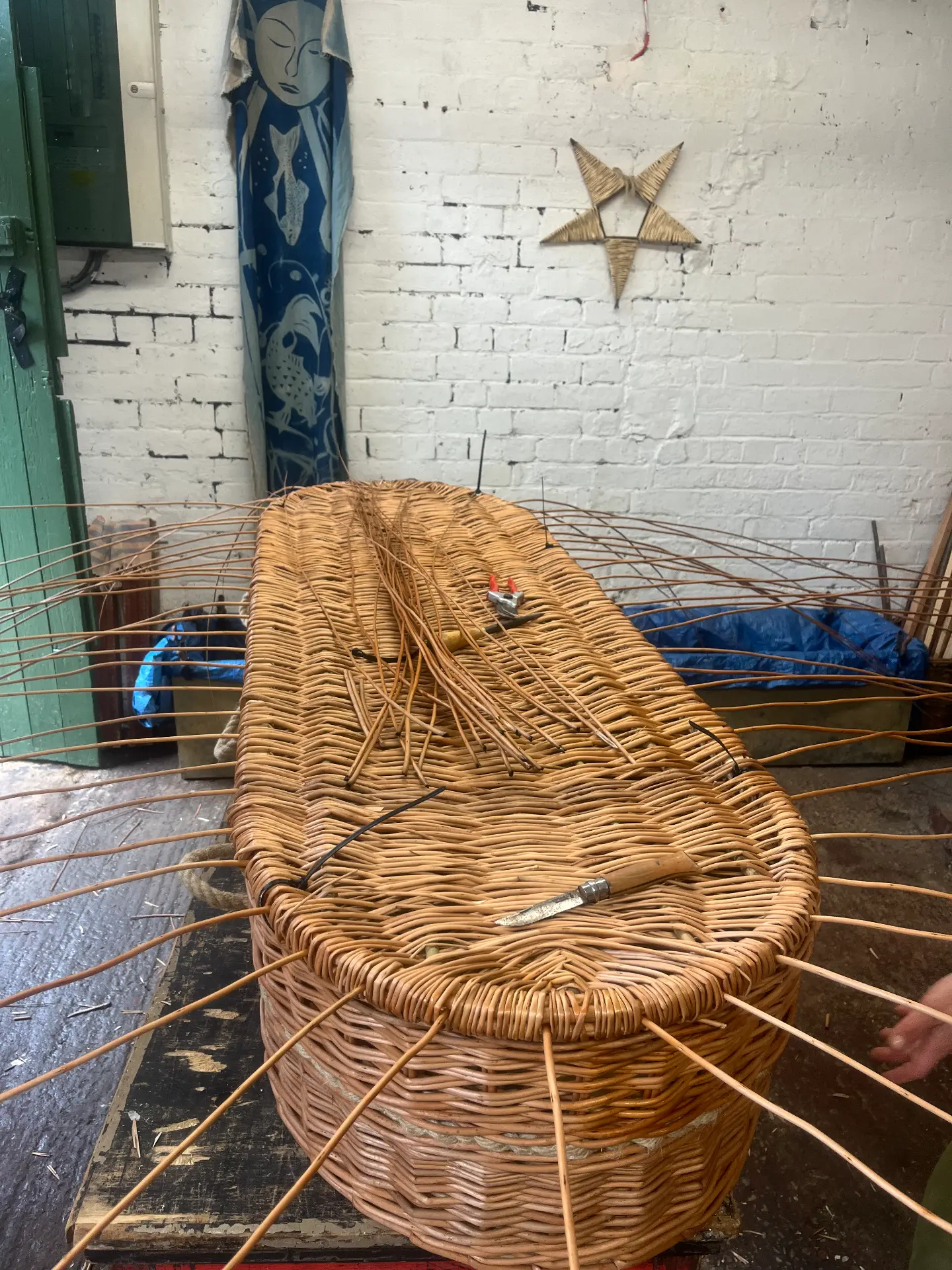 Weaving a coffin lid by hand, with tools resting on the willow